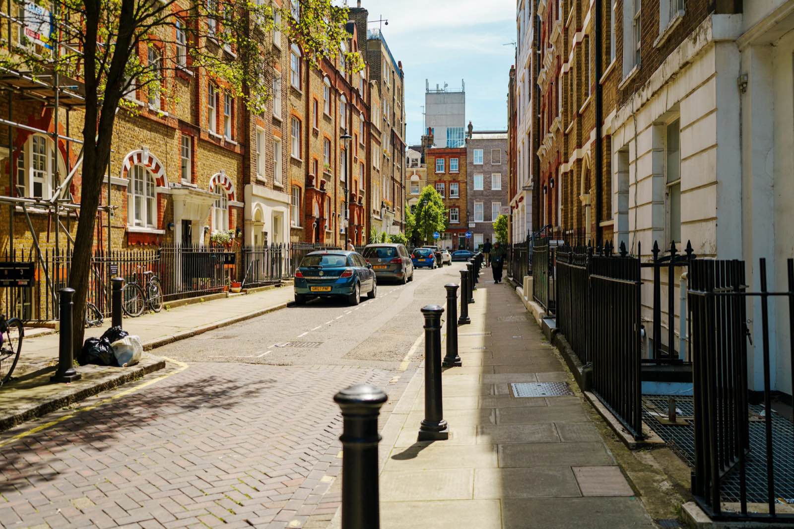 A sunny central London street lined with red-brick Victorian buildings and trees