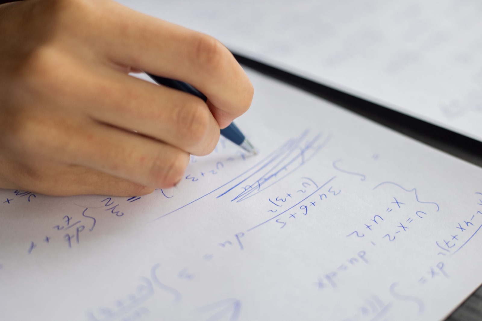 Close-up of a hand writing calculus working in blue pen on paper