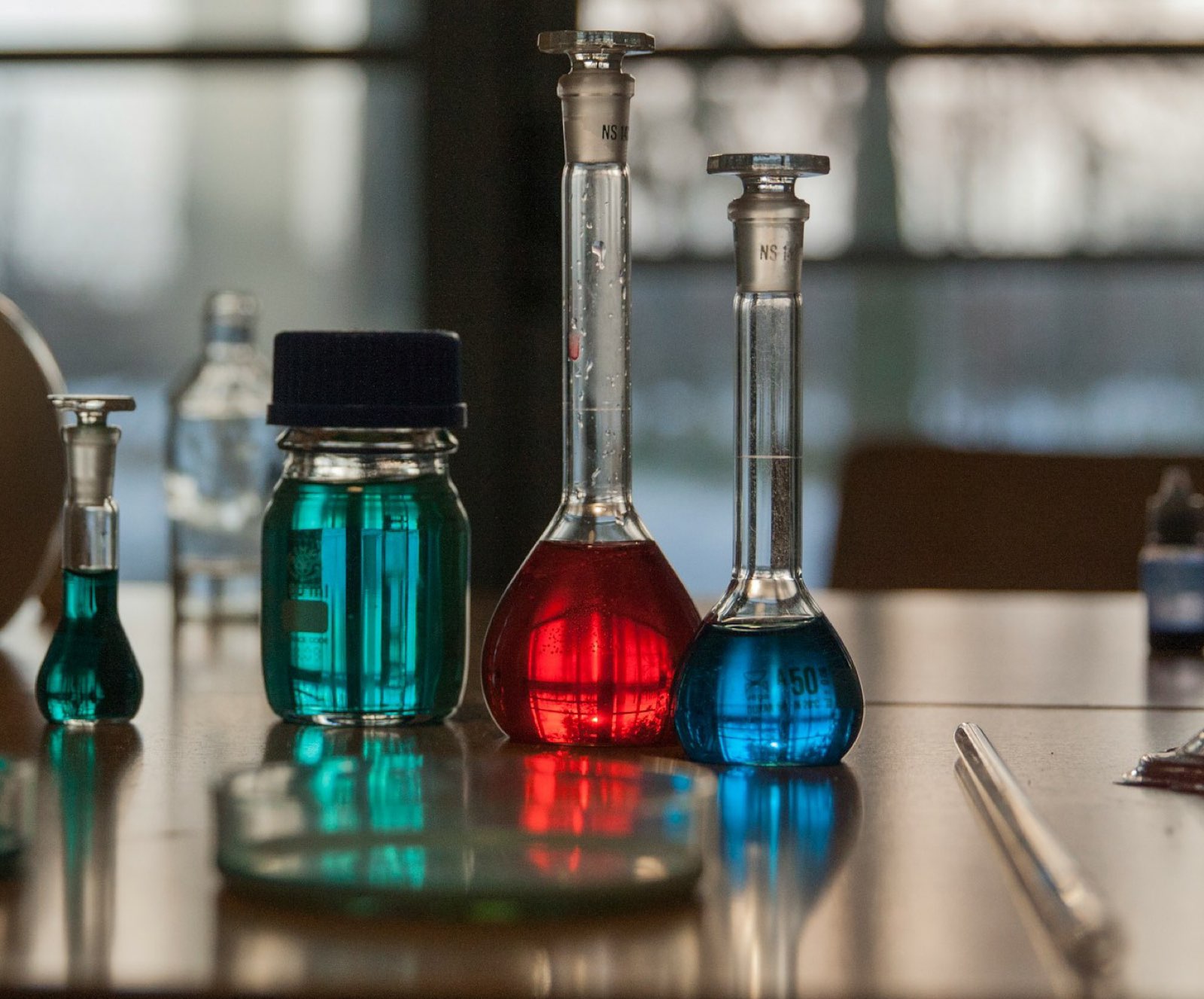 Laboratory flasks filled with red, blue and green liquids on a table by a window
